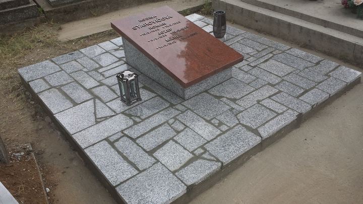 Urnový hrob s nízkym žulovým pomníkom a kamennou dlažbou.
