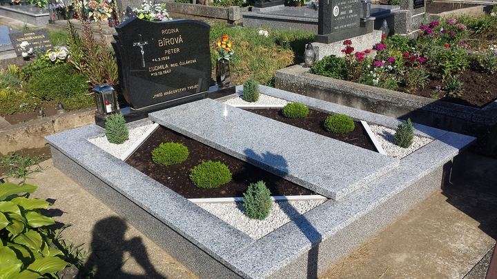 Dvojhrob zo svetlej žuly s dekoratívnou výsadbou a tmavým pomníkom.