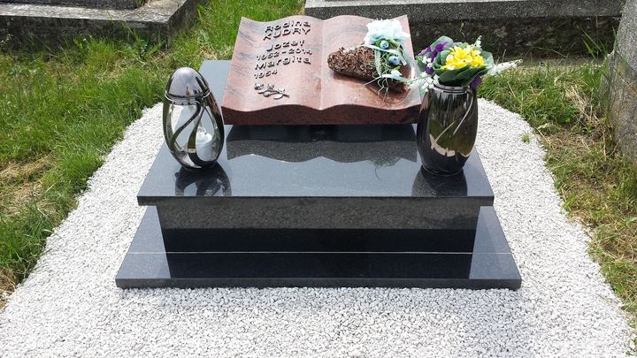 Urnový hrob s pomníkom v tvare otvorenej knihy, vázami a lešteným čiernym podstavcom.